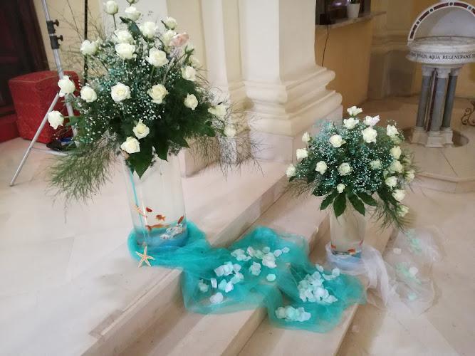 Due composizioni floreali con rose bianche e verde fiancheggiano un altare della chiesa. Tessuto drappeggiato blu e bianco con petali di rosa sparsi decora i gradini.