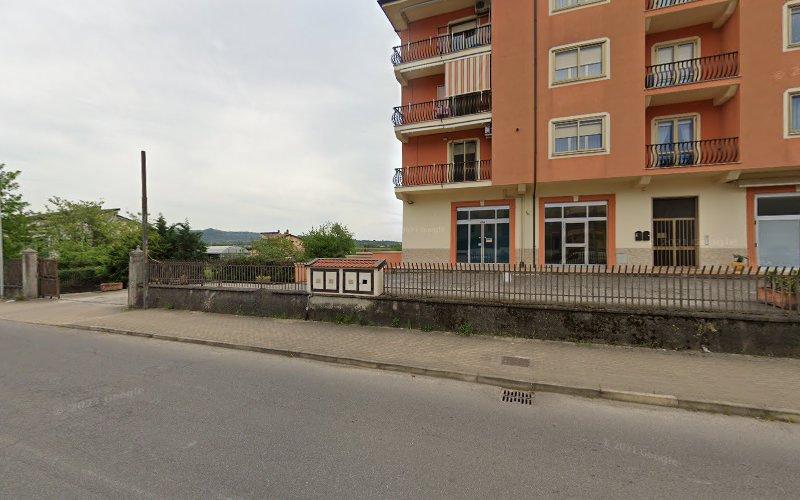 Un edificio color pesca di quattro piani con balconi sorge all'angolo di una strada. Un ingresso recintato e un piccolo cortile sono adiacenti all'edificio. La scena è tranquilla, senza pedoni o veicoli visibili.