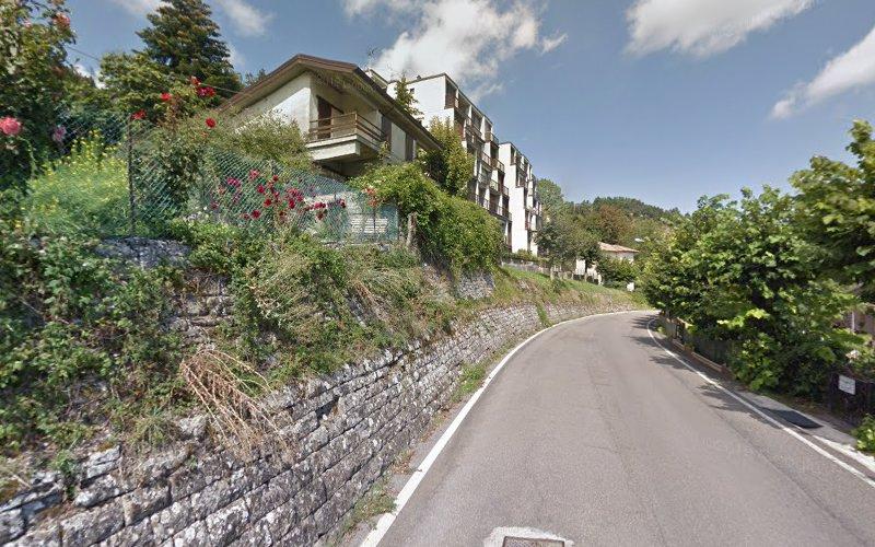 Veduta di una strada tortuosa con muri in pietra sul lato sinistro, fiancheggiata da edifici residenziali e alberi sotto un cielo parzialmente nuvoloso.