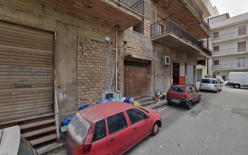 Una strada con diverse auto parcheggiate di fronte a un edificio fatiscente con una facciata parzialmente ricoperta di mattoni, porte del garage chiuse e balconi.