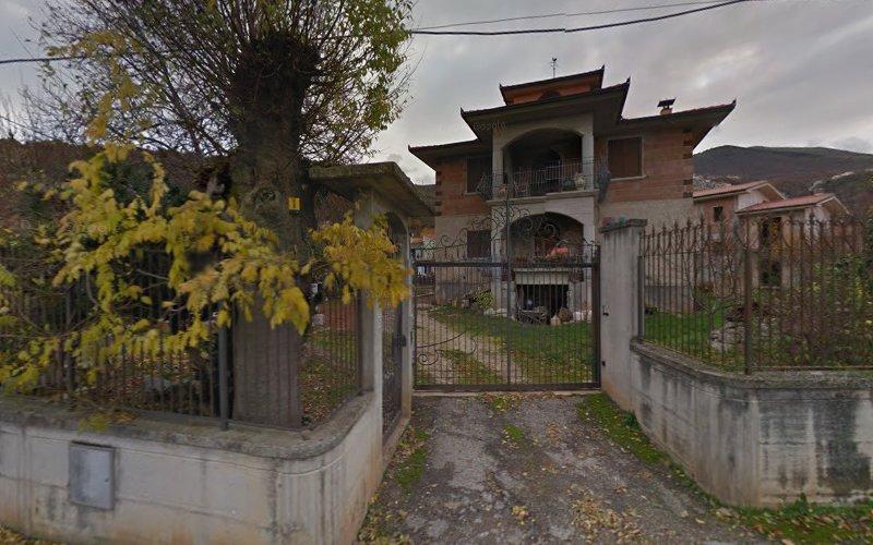 Una casa in mattoni a due piani con un vialetto d'accesso recintato, circondata da alberi e una recinzione in cemento, situata in una zona suburbana.