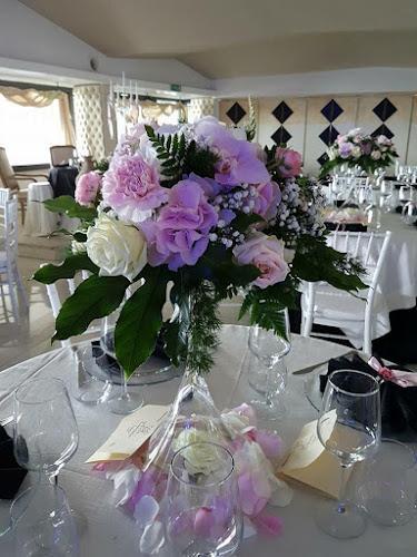 Un tavolo apparecchiato per un evento con un centrotavola floreale composto da rose rosa e bianche, circondato da calici da vino, tovaglioli piegati e petali di rosa sparsi.