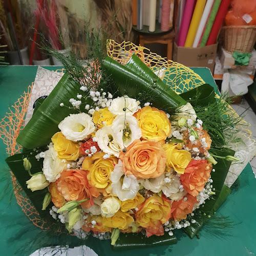 Un bouquet di rose gialle e arancioni, fiori bianchi e foglie verdi disposti su una superficie verde, con rotoli di carta da regalo e un cestino sullo sfondo.