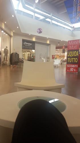 Interno di un centro commerciale con posti a sedere moderni e vetrine. I cartelli visibili includono un cartello di vendita che offre fino all'80% di sconto e un cartello del negozio "Lovera".