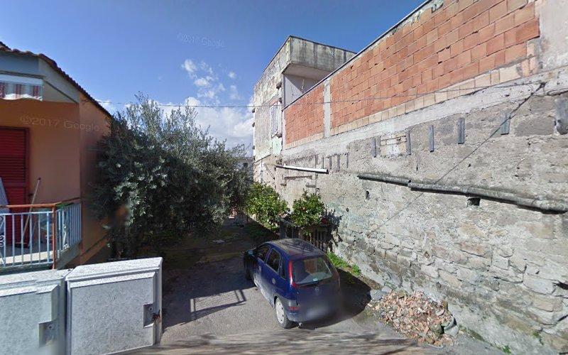 Un vicolo stretto con un'auto parcheggiata accanto a un edificio incompiuto. La zona è parzialmente ombreggiata da un albero e il cielo è limpido con nuvole sparse.