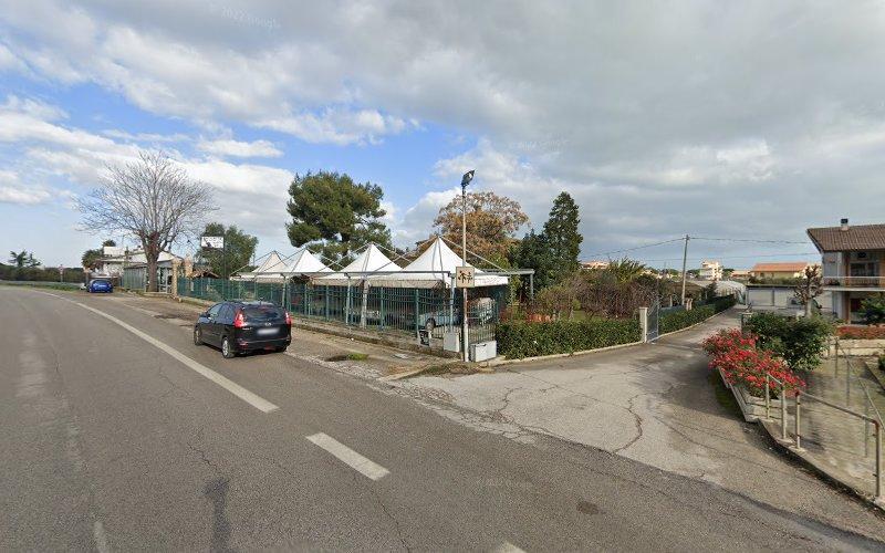 Una scena di strada con un'auto nera parcheggiata sul ciglio della strada, diverse tende bianche sullo sfondo e un cielo parzialmente nuvoloso.