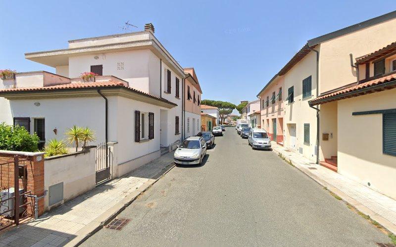 Una stretta strada residenziale con auto parcheggiate su entrambi i lati, fiancheggiata da case bianche e beige con le finestre chiuse sotto un cielo azzurro e limpido.