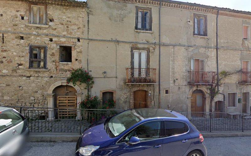 Vista stradale di un vecchio edificio in pietra con porte e balconi in legno, parzialmente coperto dal verde. Un'auto blu è parcheggiata di fronte.